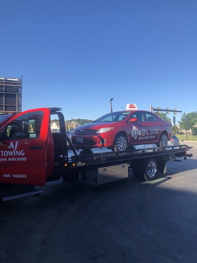 AJ Towing red flatbed truck transporting a red sedan on a clear day in Milwaukee.