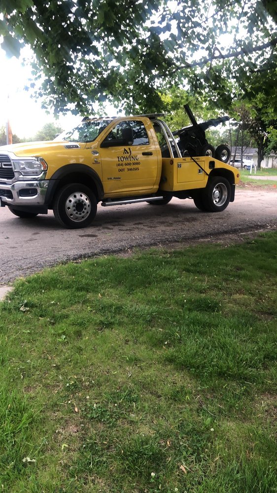 AJ Towing yellow wrecker tow truck with boom and wheel lift, lettered with the AJ Towing name and phone number.